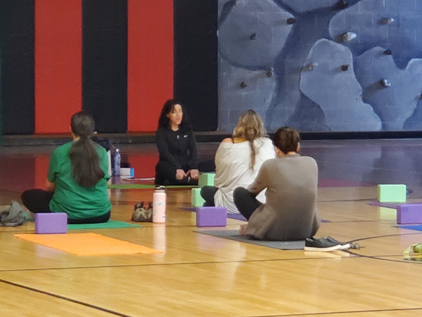 Woman leads mediation with people sitting on gym floor