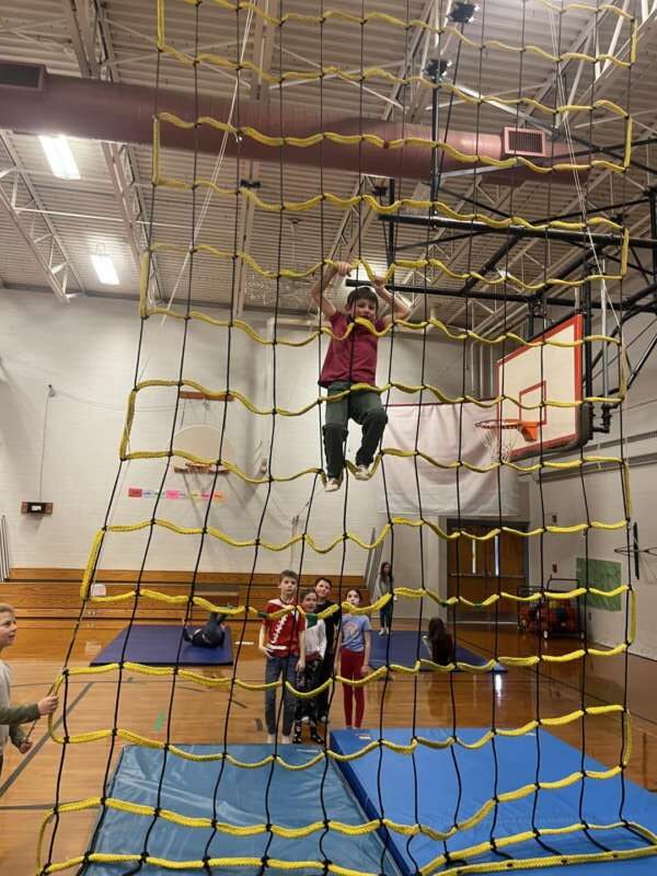 boy climbing the cargo net with other students watching