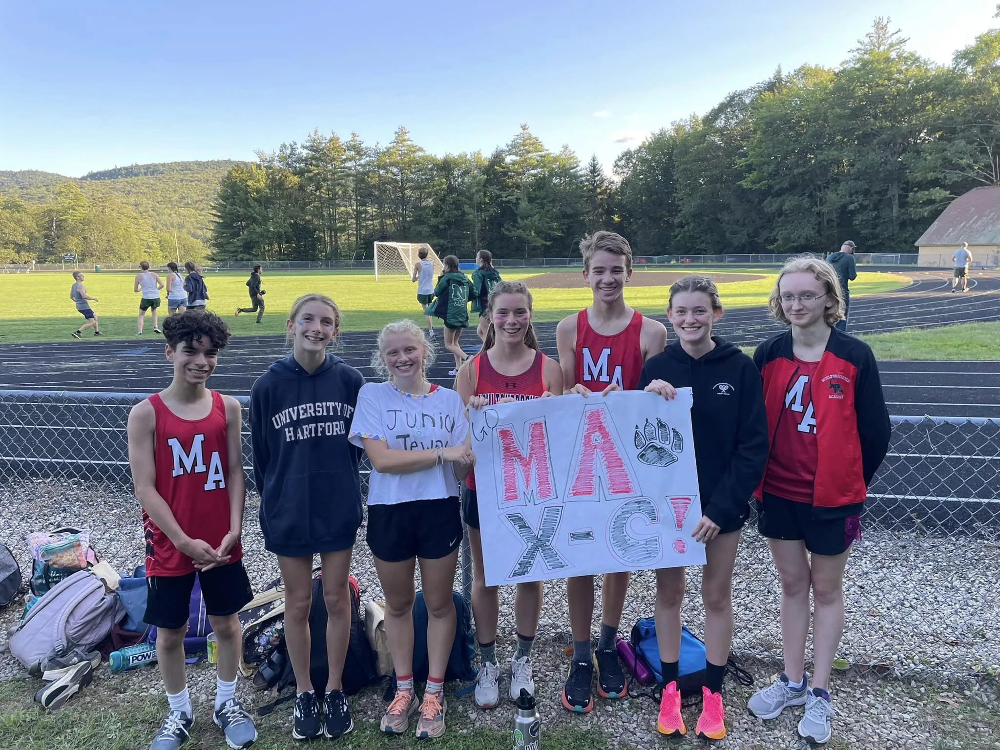 group of xc runners stadning together at the track holding a sign that says "MA XC"