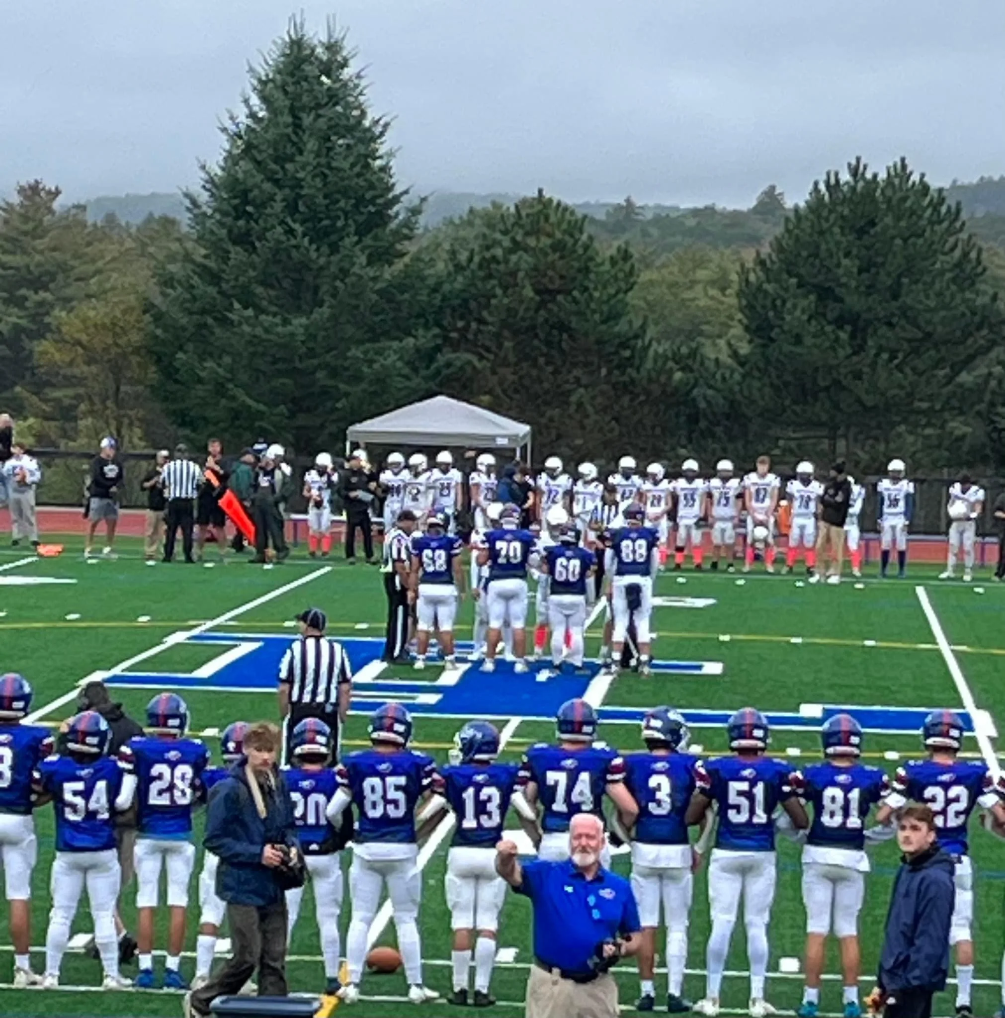 four football players at center field for coin flip with team standing on the sideline
